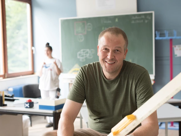 Ein Lehrer in einer CJD Christophorusschule sitzt auf einem Tisch vor der Tafel.